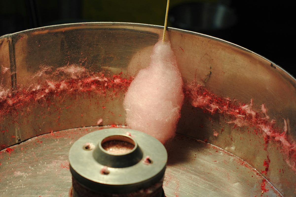 A commercial cotton candy machine spinning pink fairy floss onto a stick