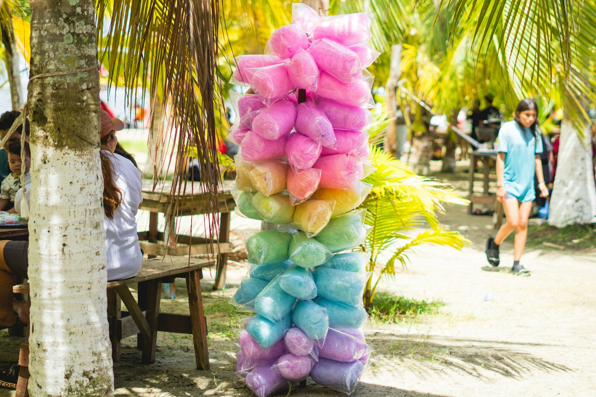 Wrapped fairy floss in pink, yellow, green, blue and purple stacked on a pole at an outdoor market